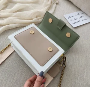 "Small, rectangular clutch bag made of smooth pu leather, with a metallic clasp on top and a detachable wrist strap. The bag is minimalist in design, featuring a single compartment and a subtle, polished finish."